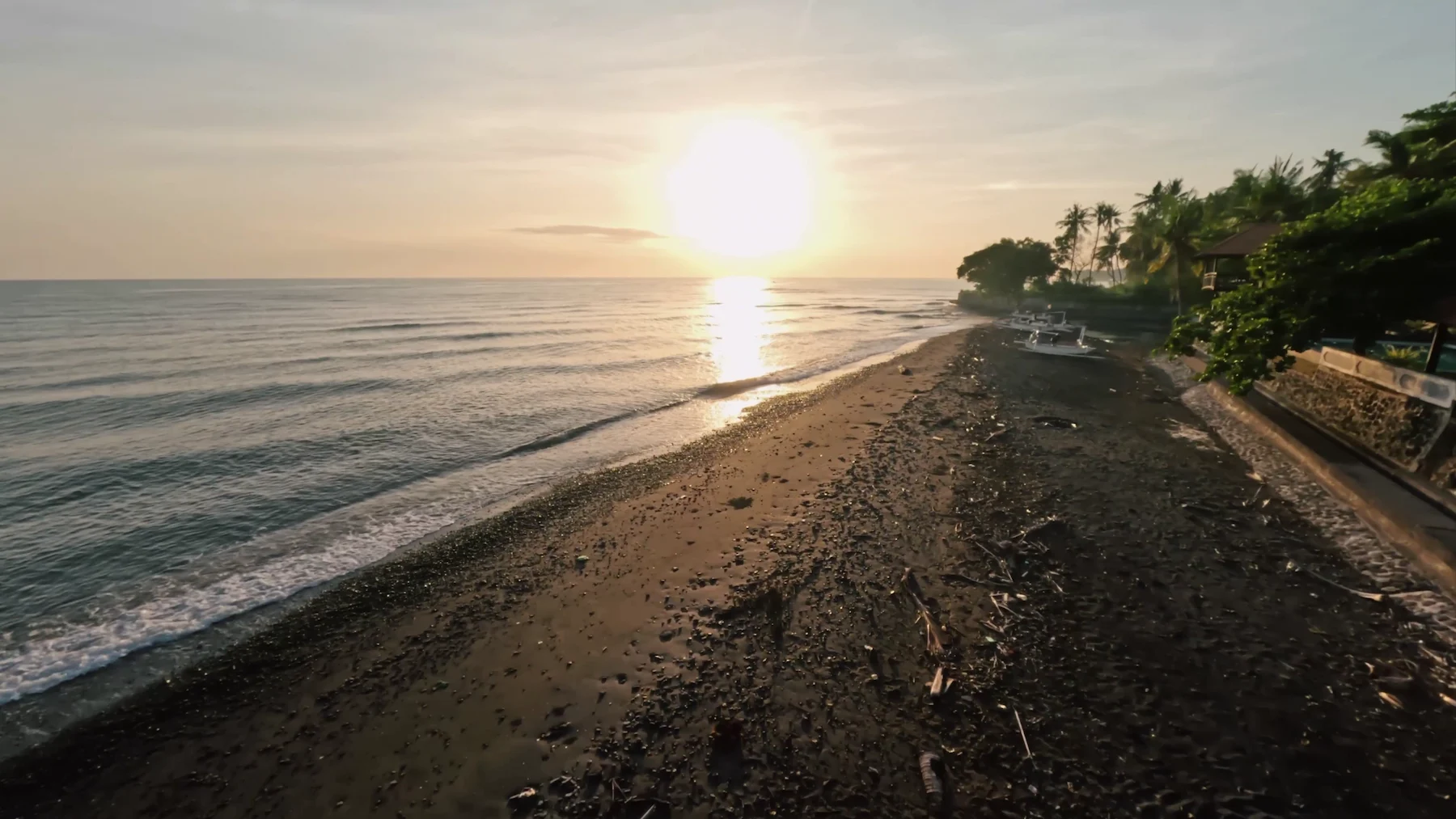 Black sand beach at sunrise with traditional Balinese outrigger boats; coastline near Primavera Beach House, North Bali.