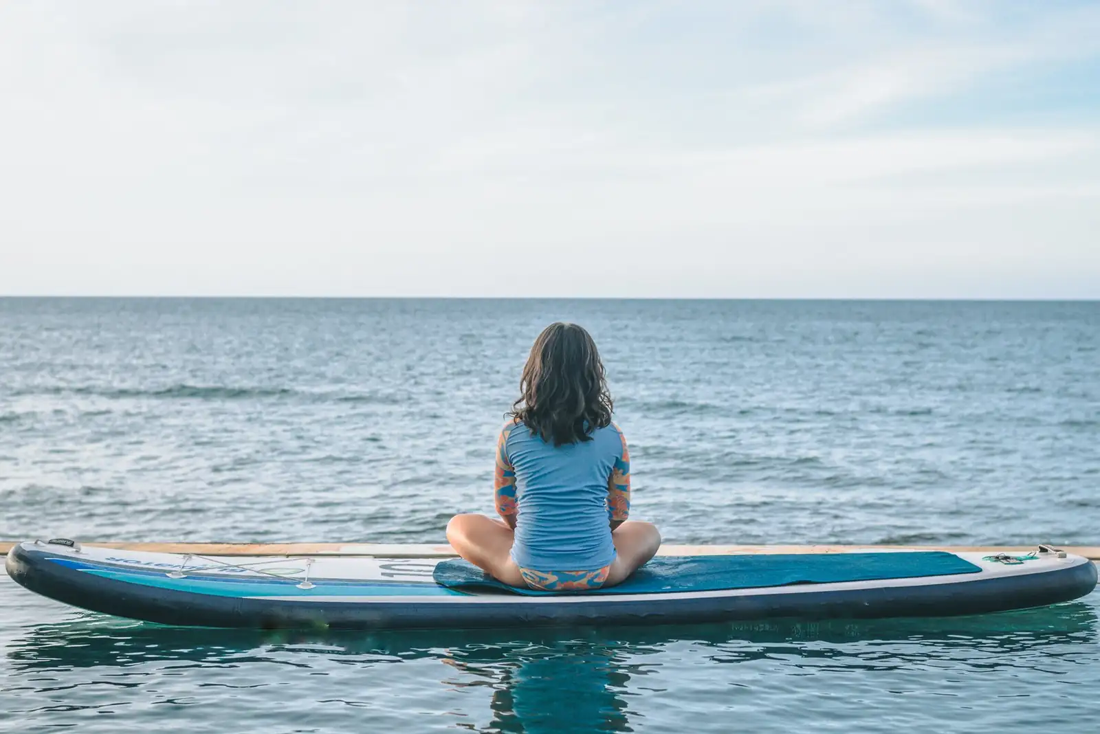 Child sitting cross-legged on a paddleboard facing the open sea in front of Primavera Beach House.