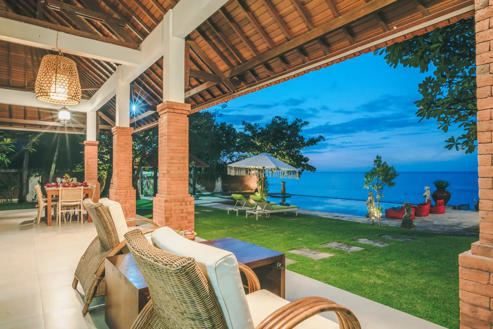 Blue hour view from the covered terrace looking out at the pool, garden, and sea.